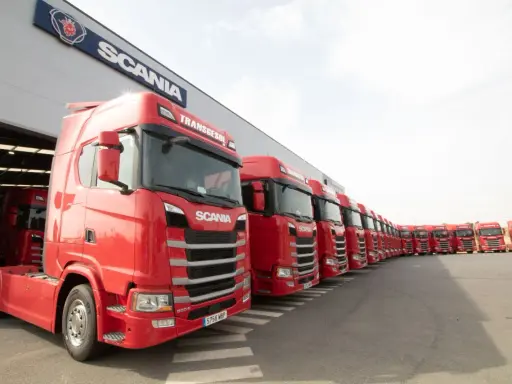 Una fila de camiones Scania rojos, listos para la acción, con el logo de Scania en el edificio.