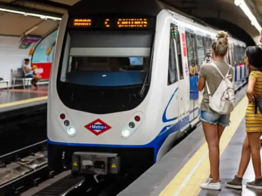 En la estación de metro, un tren blanco espera. Varias personas observan, una podría recibir una multa por usar tarjeta de transporte de otra persona.