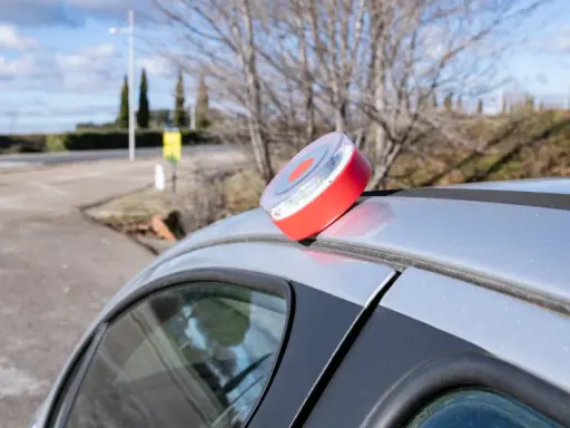 Baliza de emergencia roja y blanca en el techo de un coche plateado, lista para evitar una multa.