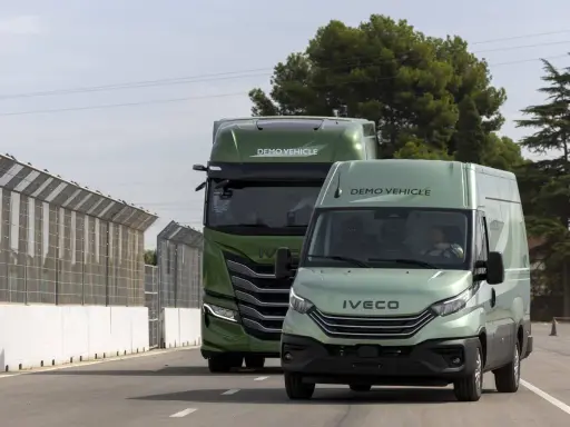 Dos vehículos Iveco, un camión y una furgoneta, ambos de color verde y con la etiqueta "DEMO VEHICLE", circulan por una carretera.