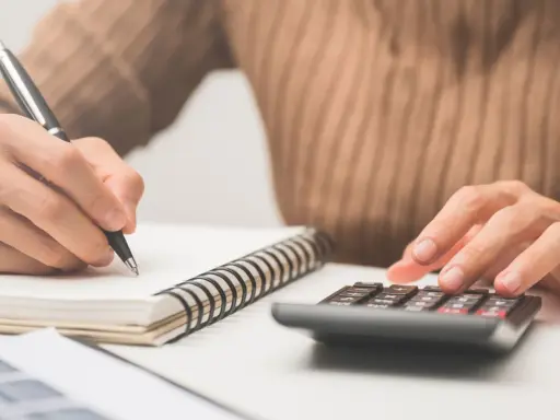 Calculando el precio de clases de conducir. Mano con bolígrafo en cuaderno y otra mano en calculadora.