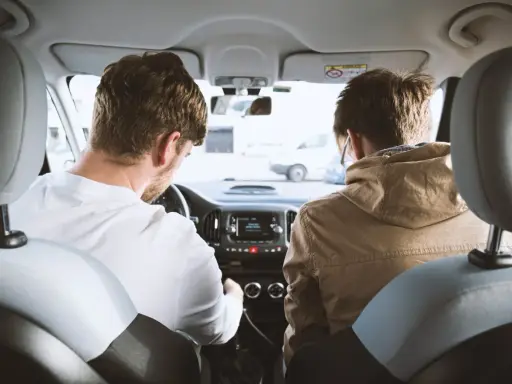 Dos hombres en un coche, uno conduce y el otro mira. Podrían estar discutiendo los tipos de faltas que se cometen al volante.
