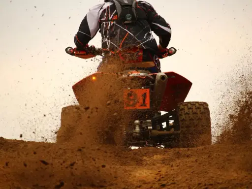 Un quad naranja con el número 1 salpica barro a máxima velocidad.