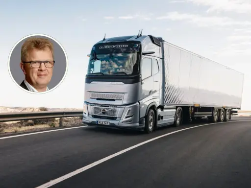 Un hombre sonríe en un círculo, mientras un camión eléctrico Volvo avanza por una carretera desértica.