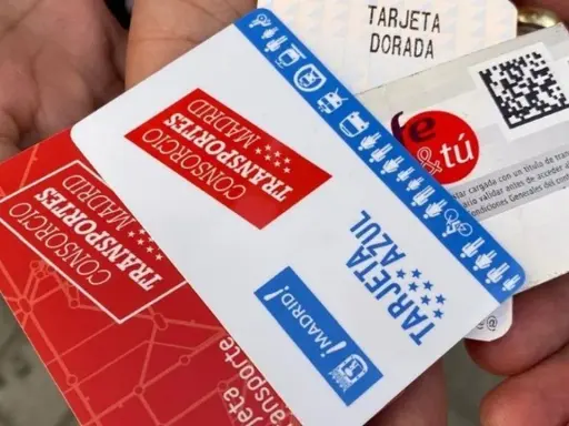 Manos sostienen varias tarjetas de transporte de Madrid, incluyendo la Tarjeta Dorada y la Tarjeta Azul, mostrando algunas excepciones de transporte.