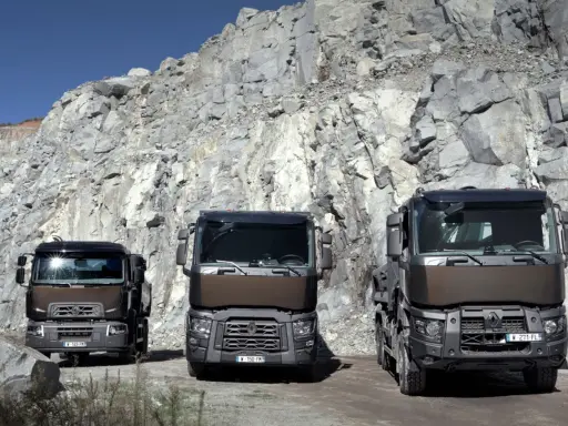 Tres robustos renault trucks modelos posan ante un imponente acantilado de cantera, listos para el trabajo pesado.