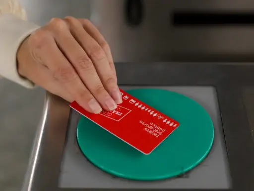 Mano acercando tarjeta roja de transporte público a un lector verde.