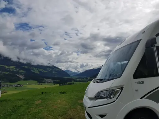 Autocaravana de más de 3500 kg aparcada en un prado verde con vistas a un valle alpino y nubes dramáticas.