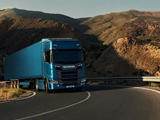 Camión Scania azul recorre una carretera sinuosa entre montañas áridas, evocando la fuerza y el espíritu de aventura de Suecia.