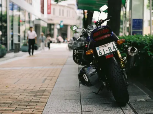 Una moto Yamaha aparcada en la acera, con dos cascos colgados. Al fondo, gente pasea por la calle.