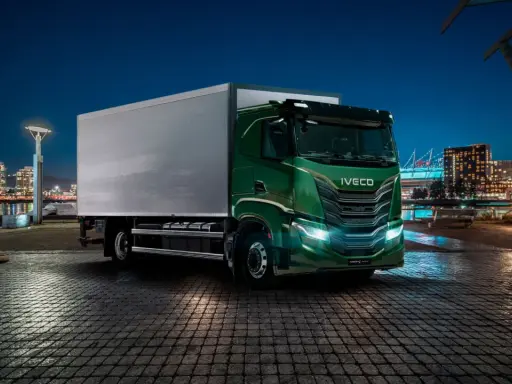 Camión Iveco S-Way V8 780 verde brillante aparcado en un muelle urbano de noche, con luces de ciudad al fondo.