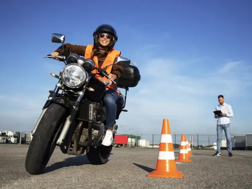 Mujer sonriente practica en circuito cerrado a1, con conos naranjas y un instructor al fondo.