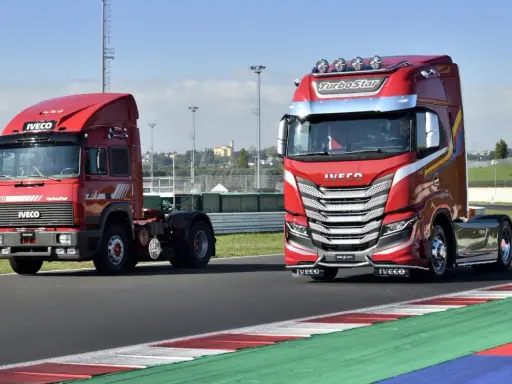 Dos camiones Iveco rojos, uno antiguo y otro moderno, en una pista de carreras.