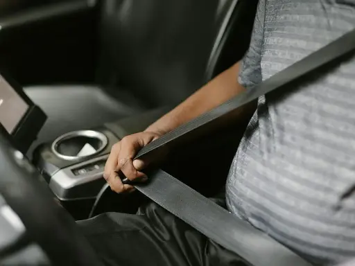 Persona se abrocha el cinturón de seguridad en un coche moderno. Las normativas de tráfico exigen que todos los pasajeros, a menos que estén exentos de llevar cinturón de seguridad, lo usen.