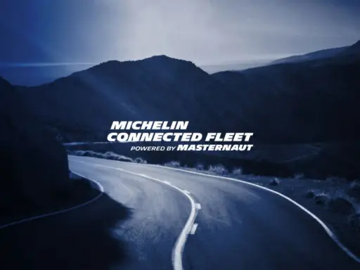Carretera sinuosa bajo un cielo azul oscuro, con el texto "MICHELIN CONNECTED FLEET" iluminado.