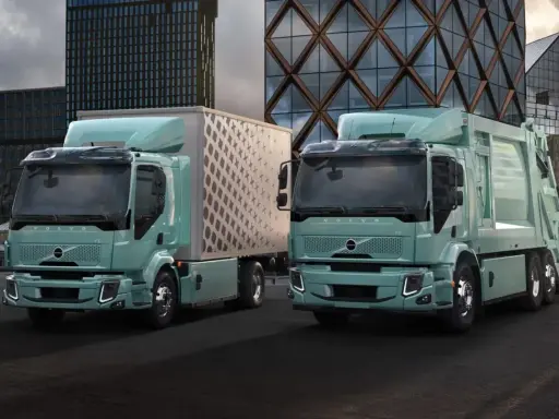 Dos camiones Volvo FE Electric, uno con caja y otro compactador, lucen modernos frente a edificios urbanos.