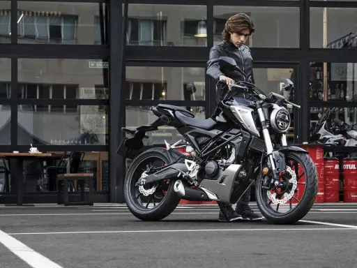Joven con chaqueta de cuero junto a una moto negra, listo para obtener su a1 permiso de conducir.