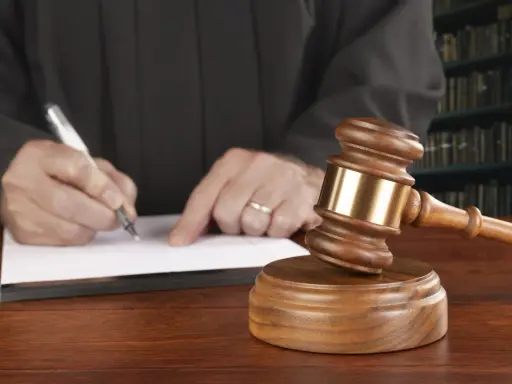 Juez firma sentencia que implica retirada carnet de conducir por curso. Martillo de juez y libros de derecho.