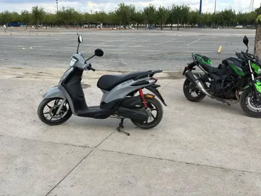 Un carnet scooter gris y dos motos verdes aparcadas en un circuito.