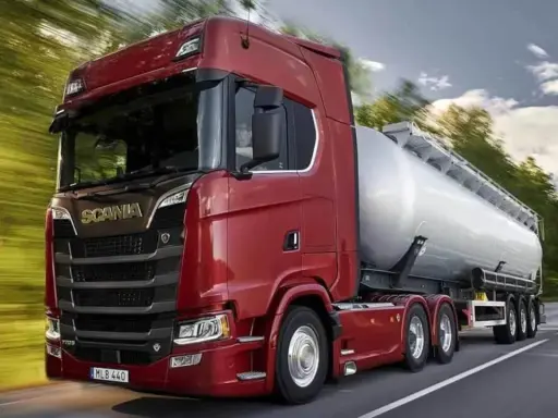 Camión cisterna Scania 800 CV de color rojo brillante, circulando por una carretera rodeada de árboles.