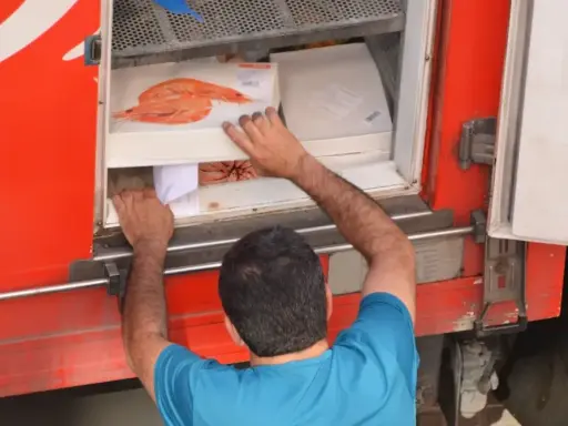 Hombre cargando cajas de camarones en un camión refrigerado, parte del transporte de alimentos por carretera.