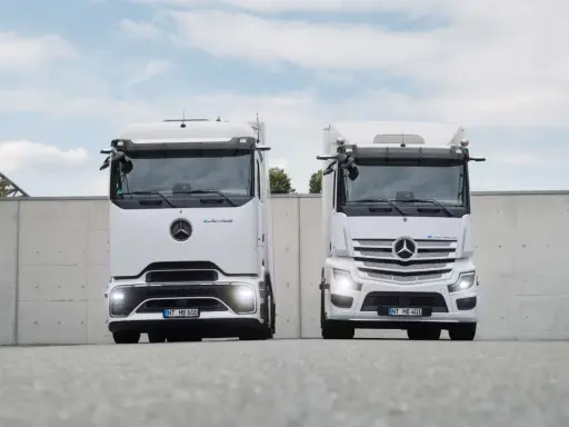 Dos camiones Mercedes-Benz eActros blancos, un nuevo camión eléctrico, se exhiben frente a un muro de hormigón.
