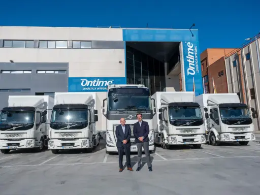 Dos hombres posan frente a una fila de camiones eléctricos de Ontime.