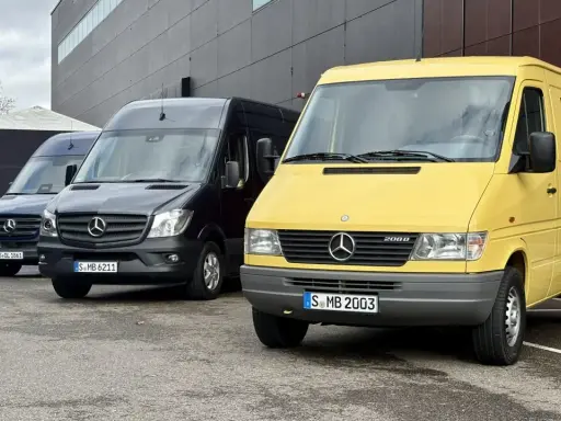 Tres furgonetas Mercedes-Benz Sprinter, una amarilla conmemorativa de 30 años, una negra y una azul, aparcadas frente a un edificio moderno.