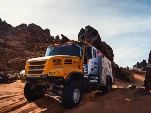 Camión Iveco Dakar amarillo compitiendo en un terreno desértico rocoso y arenoso, levantando polvo.