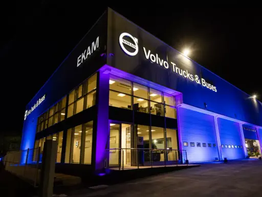 Edificio moderno de EKAM Volvo Trucks & Buses iluminado de noche con luces azules y púrpuras.