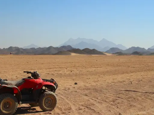 Un quad rojo, listo para la aventura, descansa en el desierto. El carnet para conducir quad 660 es tu pase a la emoción. Montañas distantes y cielo azul completan la escena.