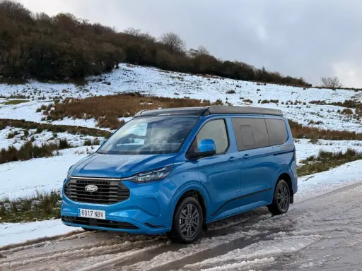 Furgoneta phev azul aparcada en un camino nevado, lista para una aventura invernal.