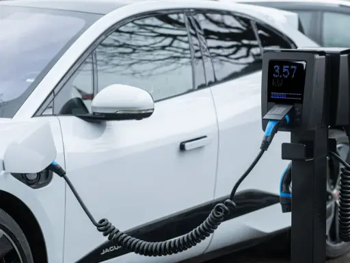 Coche eléctrico blanco cargando. El poste de carga muestra 3.57 kW, cumpliendo el reglamento AFIR para la infraestructura de energía.