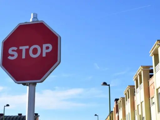 Señal de STOP roja en un poste, con edificios y cielo azul. Indica cómo hacer un stop sin visibilidad.
