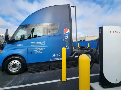 Camión semirremolque azul Pepsi junto a un cargador Tesla.
