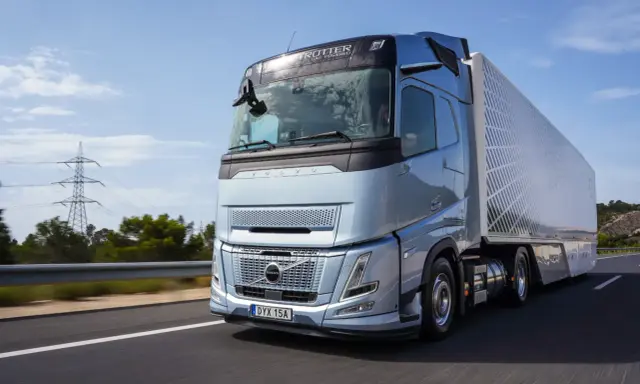 El nuevo Volvo FH Aero, un camión azul metálico, avanza por una carretera soleada, listo para transportar cargas con su diseño aerodinámico.