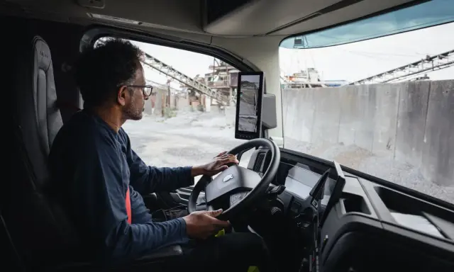 Interior de un camion Volvo. Un hombre con gafas conduce, observando las cámaras de visión.