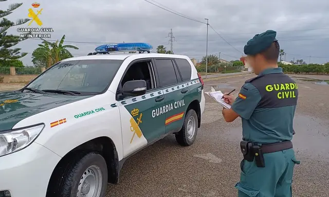 Agente de la Guardia Civil anota datos junto a un vehículo oficial. Se pregunta qué carnet se necesita para conducir un minibus.