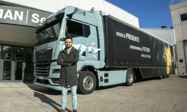 Hombre posa frente a un camión eléctrico MAN, como en las revistas de camiones. El remolque tiene un león y el lema "Construimos el futuro".