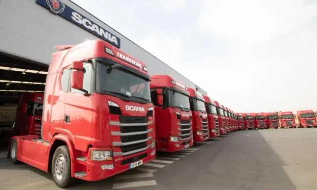 Una fila de camiones Scania rojos, listos para la acción, con el logo de Scania en el edificio.