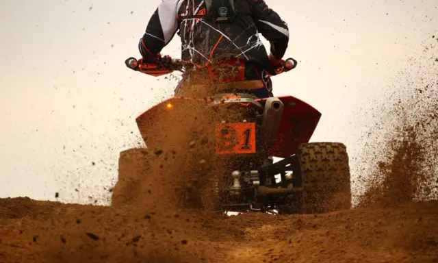 Un quad naranja con el número 1 salpica barro a máxima velocidad.