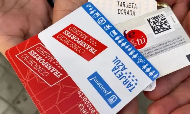 Manos sostienen varias tarjetas de transporte de Madrid, incluyendo la Tarjeta Dorada y la Tarjeta Azul, mostrando algunas excepciones de transporte.