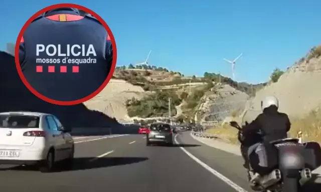 Un motorista de los Mossos d'Esquadra circula por el arcén de una autopista, adelantando a otros vehículos en un día soleado.