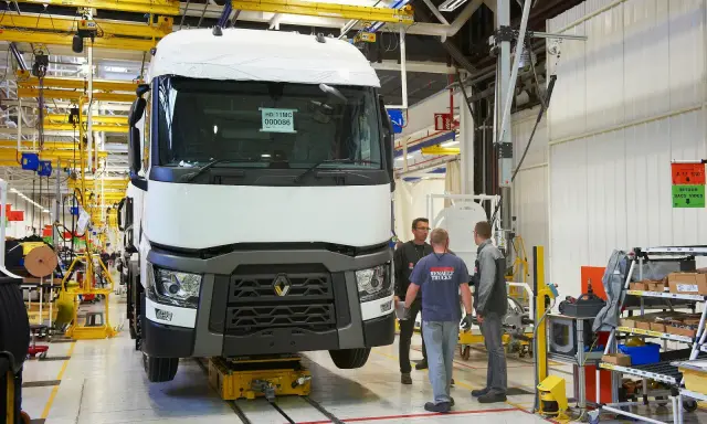 Tres trabajadores observan un camión Renault en una línea de montaje. El camión está sobre una plataforma amarilla.