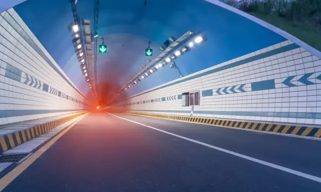 El efecto túnel se percibe al entrar en este túnel vial iluminado, con luces verdes y un resplandor rojo al fondo.