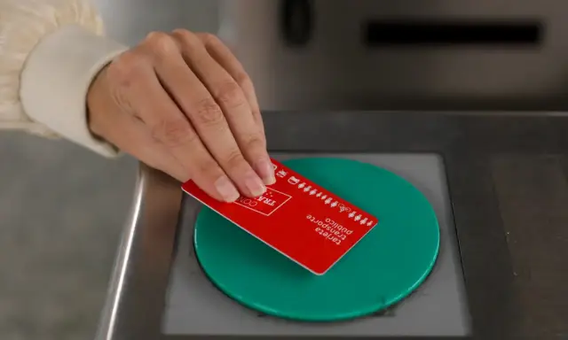 Mano acercando tarjeta roja de transporte público a un lector verde.