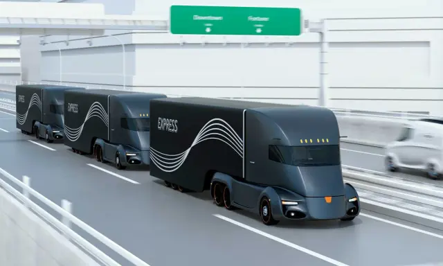 Tren de camiones del futuro, negros y aerodinámicos, circulando por una autopista.