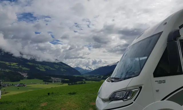 Autocaravana de más de 3500 kg aparcada en un prado verde con vistas a un valle alpino y nubes dramáticas.
