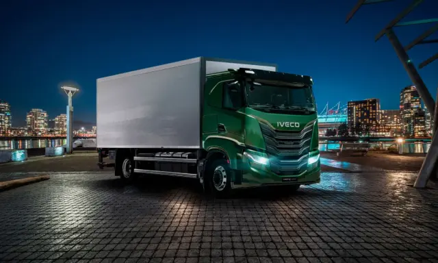 Camión Iveco S-Way V8 780 verde brillante aparcado en un muelle urbano de noche, con luces de ciudad al fondo.