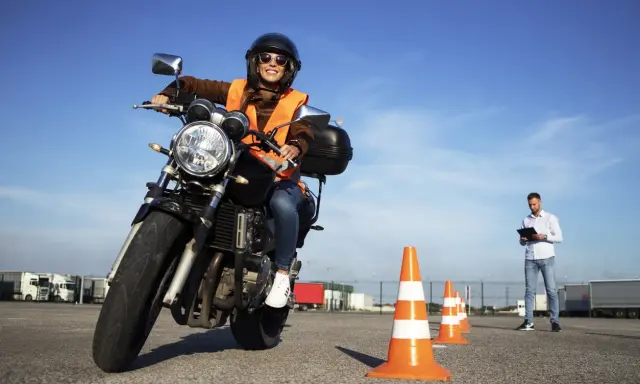 Mujer sonriente practica en circuito cerrado a1, con conos naranjas y un instructor al fondo.